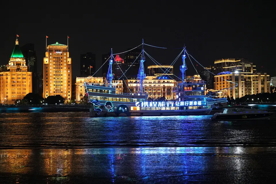 黄浦江夜游游船驶过外滩，陆家嘴天际线灯光倒映江面